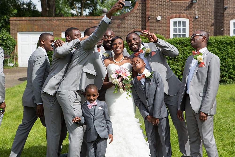 Bride and groom together with a group of men taking selfies outside