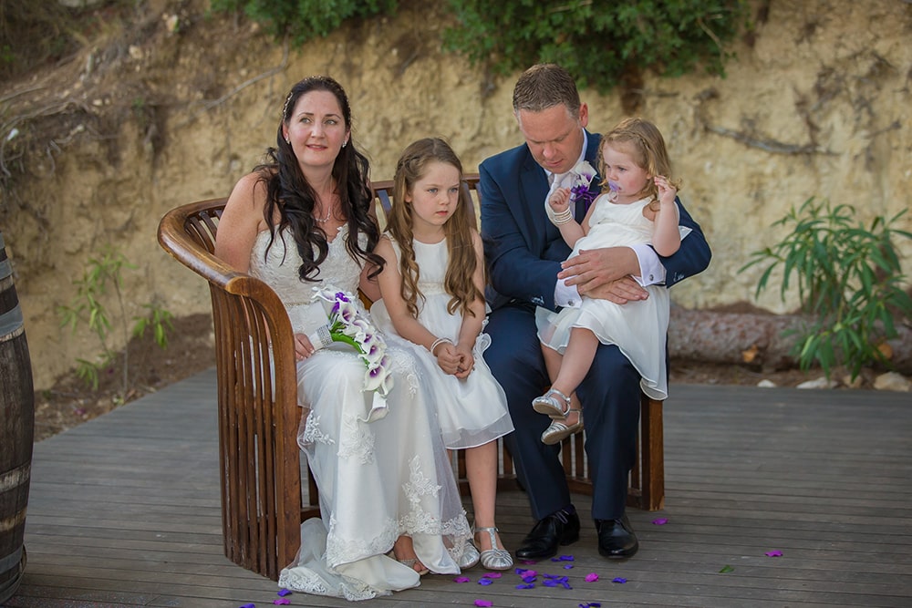 Bride and groom sitting on a bench with two little girls